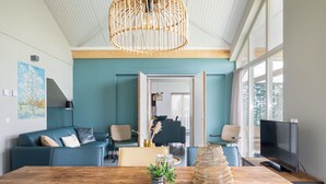 Un salon moderne avec une table à manger en bois, des canapés bleus et un grand téléviseur.