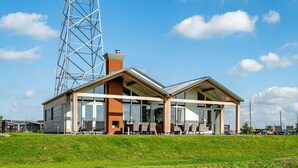 Un bâtiment moderne doté d’une façade en verre, d’une cheminée en briques et d’un espace extérieur aménagé avec des sièges.