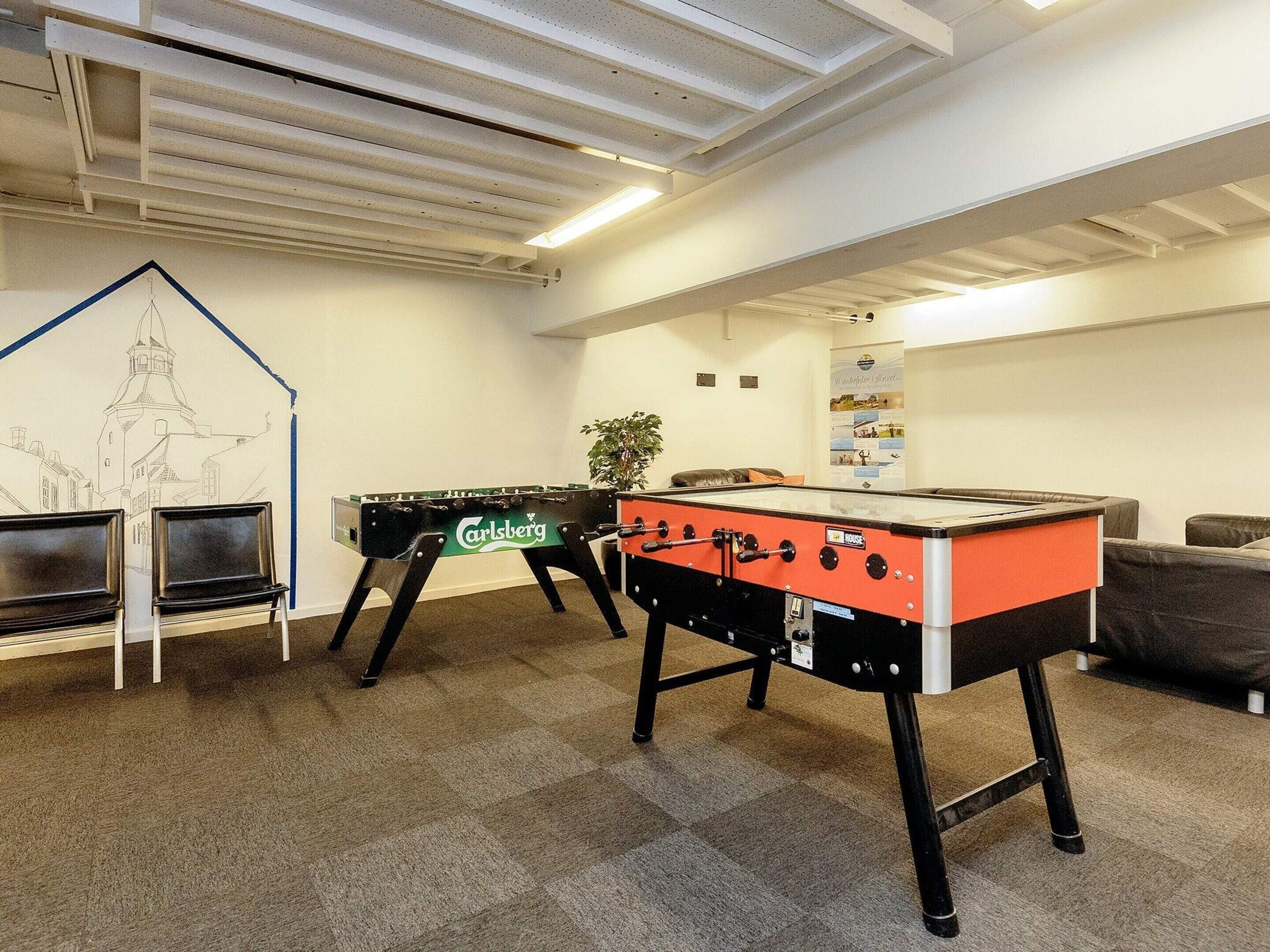 A room with two foosball tables, a wall mural, and a seating area.