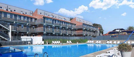 A swimming pool with lounge chairs and a building with multiple balconies in the background.