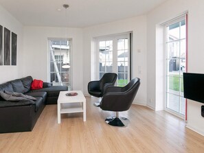 Un salon moderne avec un canapé en cuir noir, une table basse blanche et deux fauteuils noirs. Une grande fenêtre offre une vue sur l’extérieur.