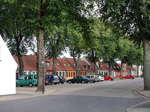 En bostadsgata med bilar parkerade längs vägen och hus med röda tak.