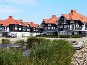 Une rangée de maisons aux façades noires et blanches, coiffées de toits rouges, un petit étang et une rive rocheuse.