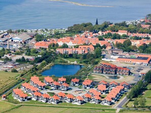 Ett flygbildsbild av ett bostadsområde vid kusten med hus som har röda tak, en liten sjö och ett kyrktorn.