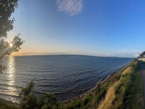 Une vue sur la côte, avec un ciel dégagé, une mer calme et un sentier herbeux longeant le rivage.