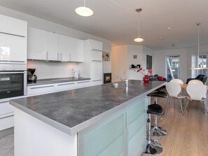 A modern kitchen with white cabinets, a large island, bar stools, and a dining area with a table and chairs.