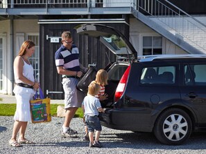 Une famille avec un enfant dans le coffre d’une voiture, un bâtiment avec un escalier et un panneau indiquant le chiffre 1.