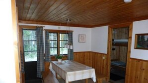 A room with a wooden ceiling, a dining table with a white tablecloth, a bench, and a window with curtains. - 4 Person Holiday Home in Torsby (Torsby)