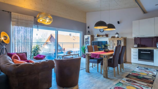 Un salon moderne comprenant un canapé, des fauteuils, une table à manger et un coin cuisine avec des placards et une cuisinière.