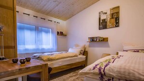 Une chambre avec deux lits, un bureau en bois, une fenêtre avec des rideaux et une étagère remplie de livres.