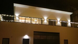 Un bâtiment moderne doté d’un grand portail de garage, d’une petite porte et d’un balcon décoré de guirlandes lumineuses.