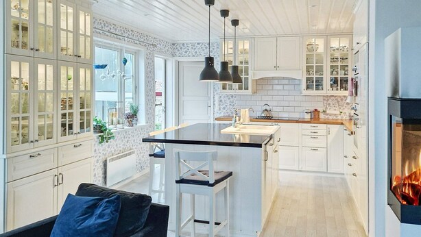 A modern kitchen with white cabinetry, a central island, pendant lighting, and a fireplace. - 9 Person Holiday Home in Tjodalyng-by Traum (Larvik)
