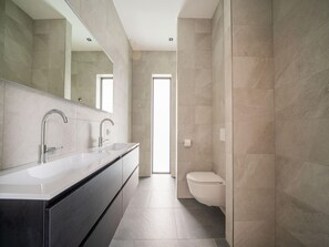 A modern bathroom with a dual sink vanity, a large mirror, and a toilet.