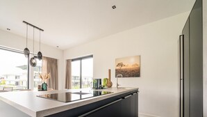 Een moderne keuken met een groot eiland, donkere kasten en een uitzicht op de buitenomgeving door grote ramen.