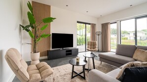 Een moderne woonkamer met een flatscreen televisie, een bank, een fauteuil, een salontafel en een grote plant.