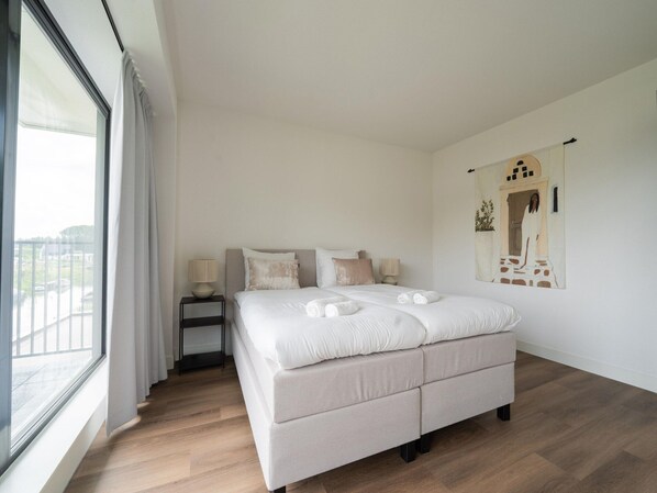 A bedroom with a large bed, a nightstand, a lamp, and a painting on the wall.