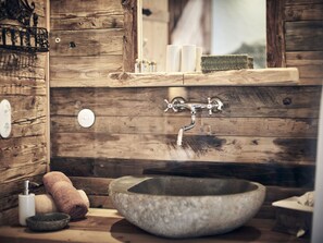A rustic bathroom with a stone sink, wooden walls, a mirror, and toiletries. - Rustic Holiday Home With Sauna (Graen)