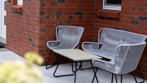 A brick wall with two grey wicker chairs and a small table. - Holiday Home Nige Og (Cuxhaven)