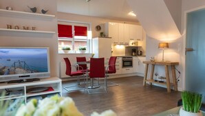 A modern living room with a television, red chairs, a dining table, and a kitchen area with white cabinets and red accents. - Holiday Home Nige Og (Cuxhaven)