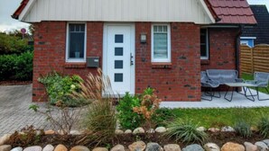 A two-story house with a red-tiled roof, a white front door, and a small garden with a stone wall in front. - Holiday Home Nige Og (Cuxhaven)