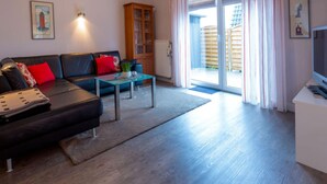 A living room with a black sofa, red cushions, a glass coffee table, and a wooden cabinet. - Holiday Home Nige Og (Cuxhaven)