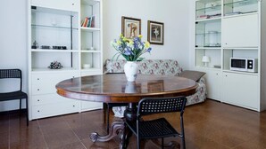 A dining area with a round wooden table, two chairs, a vase with flowers, a sofa, and a white bookshelf. - Quiet and secluded, close to Cinque Terre, Porto Venere, Lerici, and Tellaro (Le Grazie)