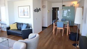 A modern living room with a sofa, chairs, a dining table, and a kitchen area in the background. - Apartment in Nieuwpoort With sea View (Nieuwpoort)