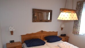 A bedroom with a wooden bed frame, two pillows, a bedside table with a lamp, and a mirror on the wall. - Gemutlicher Fussener Ruckzugsort in der Nahe des Sees (Fuessen)