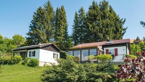 A modern house with a white exterior and red shutters, surrounded by lush greenery and tall trees. - Gemutlicher Fussener Ruckzugsort in der Nahe des Sees (Fuessen)