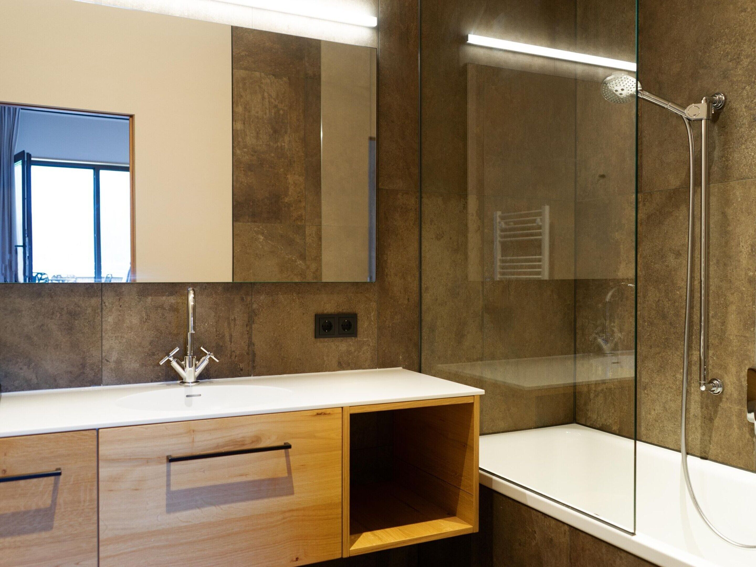 A modern bathroom with a large mirror, a shower enclosure, and a vanity with a sink and wooden cabinets.