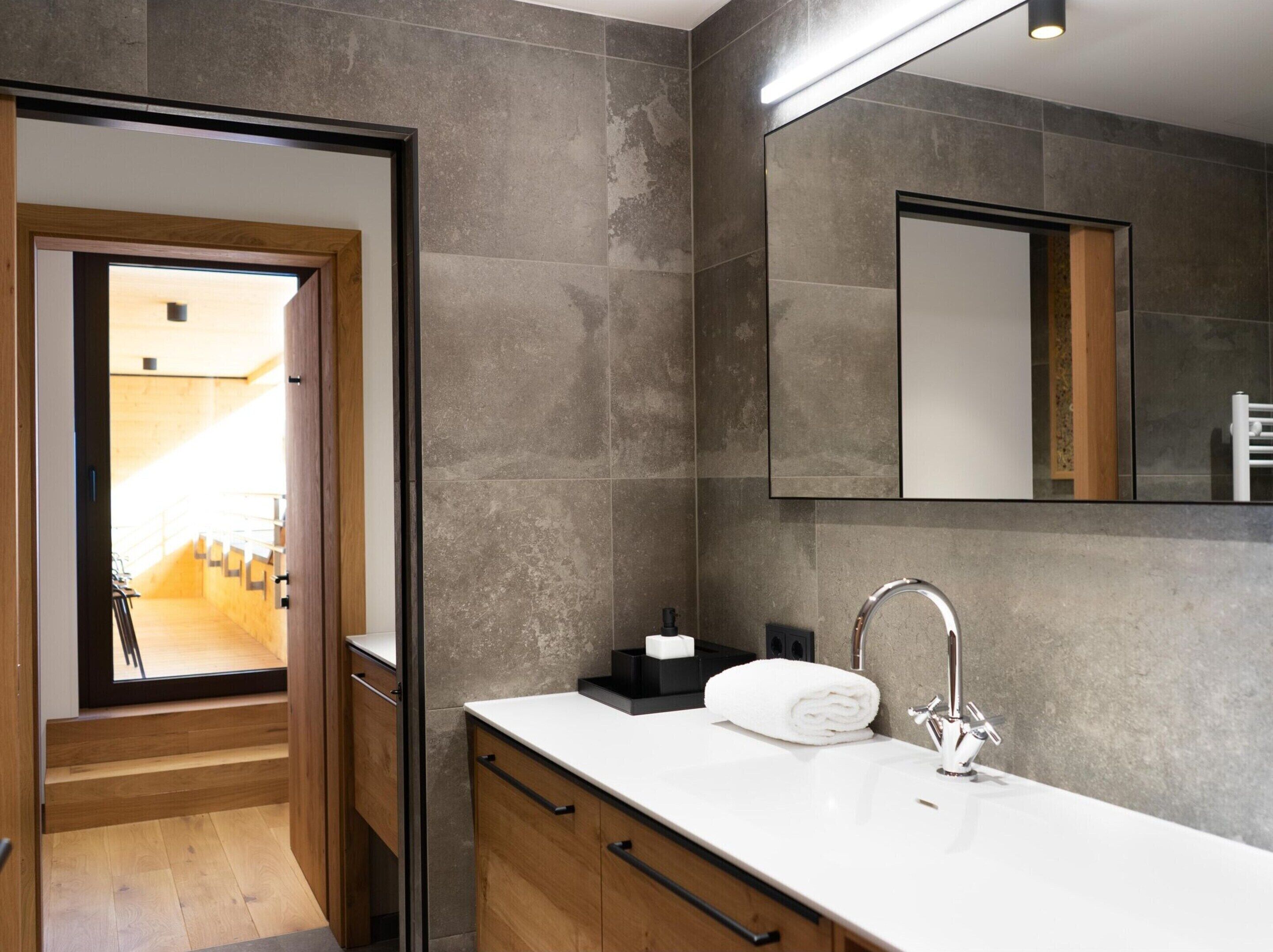 Une salle de bain moderne avec un grand miroir, un plan de toilette blanc et une serviette.