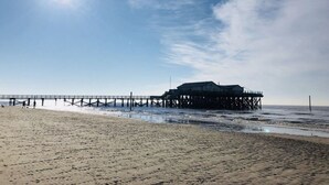 A beach with a pier extending into the sea, featuring a building on stilts. - Nordseelodge Comfortable Holiday Residence (Tetenbüll)