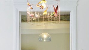 A room with a white chair, a hanging birdcage, and a pendant light. - Nordseelodge Comfortable Holiday Residence (Tetenbüll)