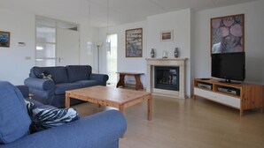Un salon comprenant un canapé, une table basse, une cheminée, un meuble pour la télévision et des œuvres d’art accrochées aux murs.