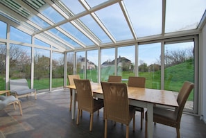 A conservatory with a glass roof, a wooden table, and wicker chairs. - Beautiful Villa With Winter Garden (Makkum)