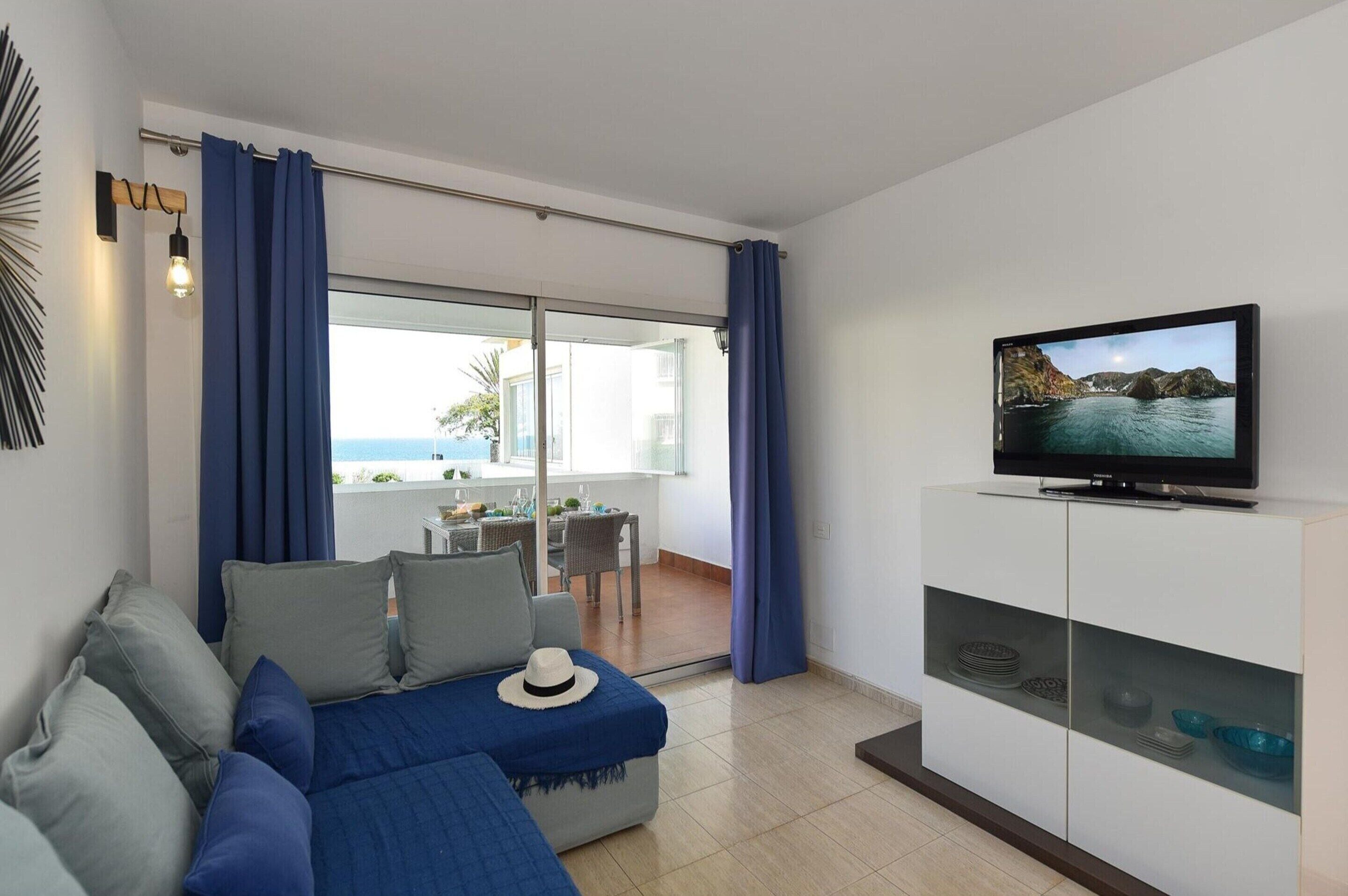 Ein modernes Wohnzimmer mit einer Couch, einem Fernseher und Blick ins Freie.