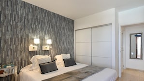 Une chambre d’hôtel moderne avec un grand lit, deux lampes de chevet, une armoire et un miroir au mur.