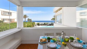 Un coin repas avec une table dressée pour deux personnes, offrant une vue sur la piscine et l’océan.