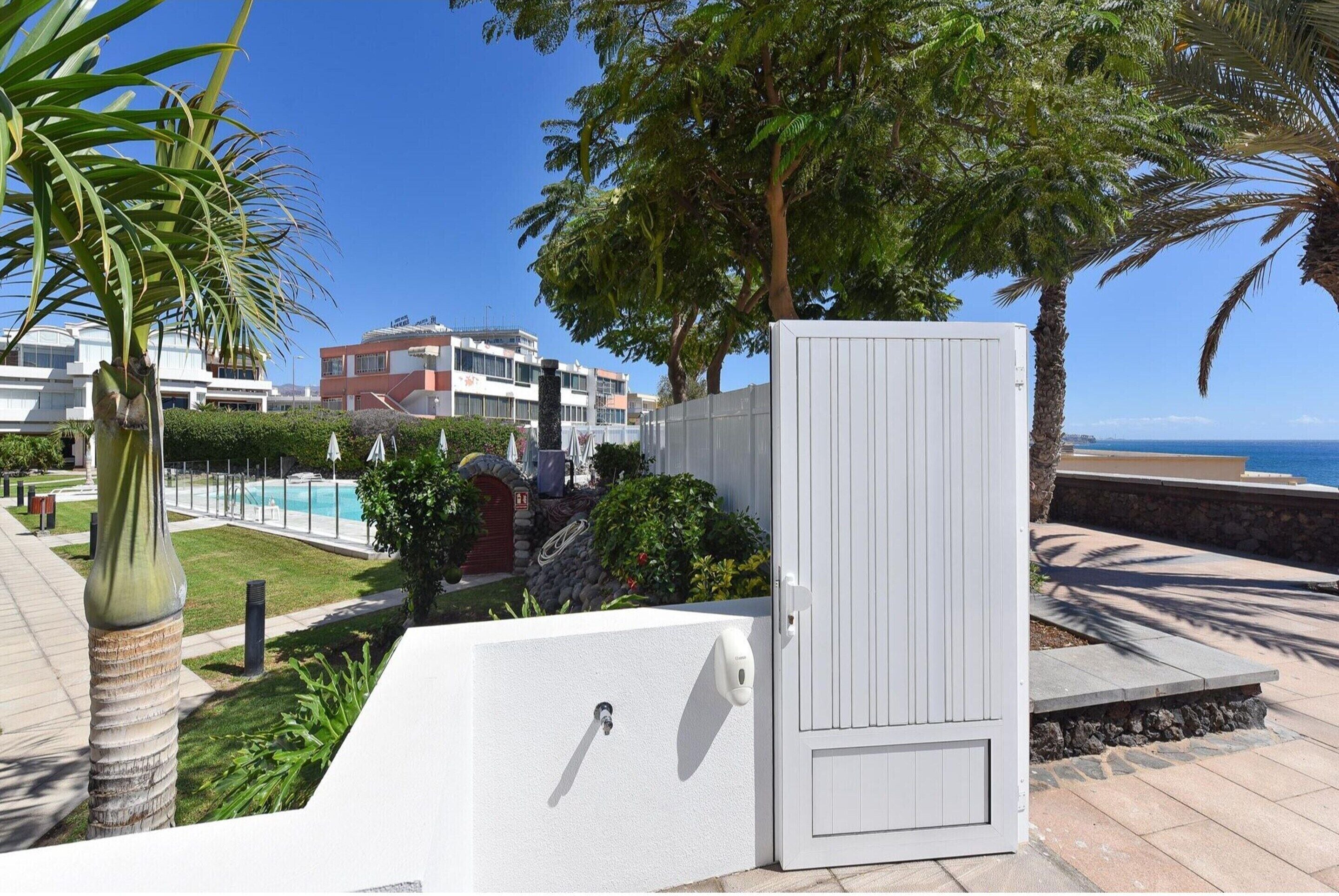 A gated area with a pool, palm trees, and a view of the ocean.