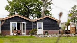 A two-story building with a dark exterior, a white door, and a small patio with chairs. - Rural Holiday Home With Large Terrace (Hellendoorn)