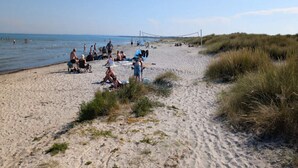 Een zandstrand met mensen die ontspannen en een volleybalnet in de verte.