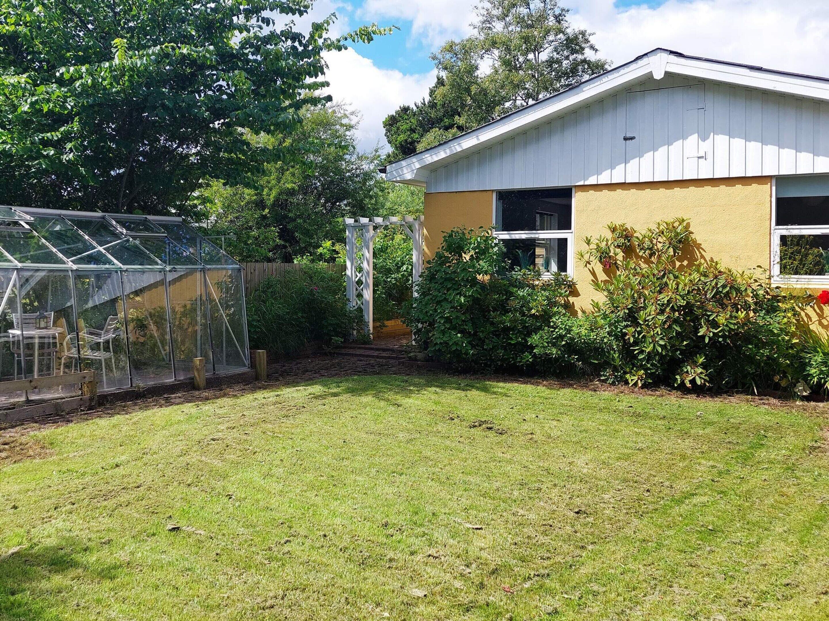 A house with a garden, a greenhouse, and a white fence.