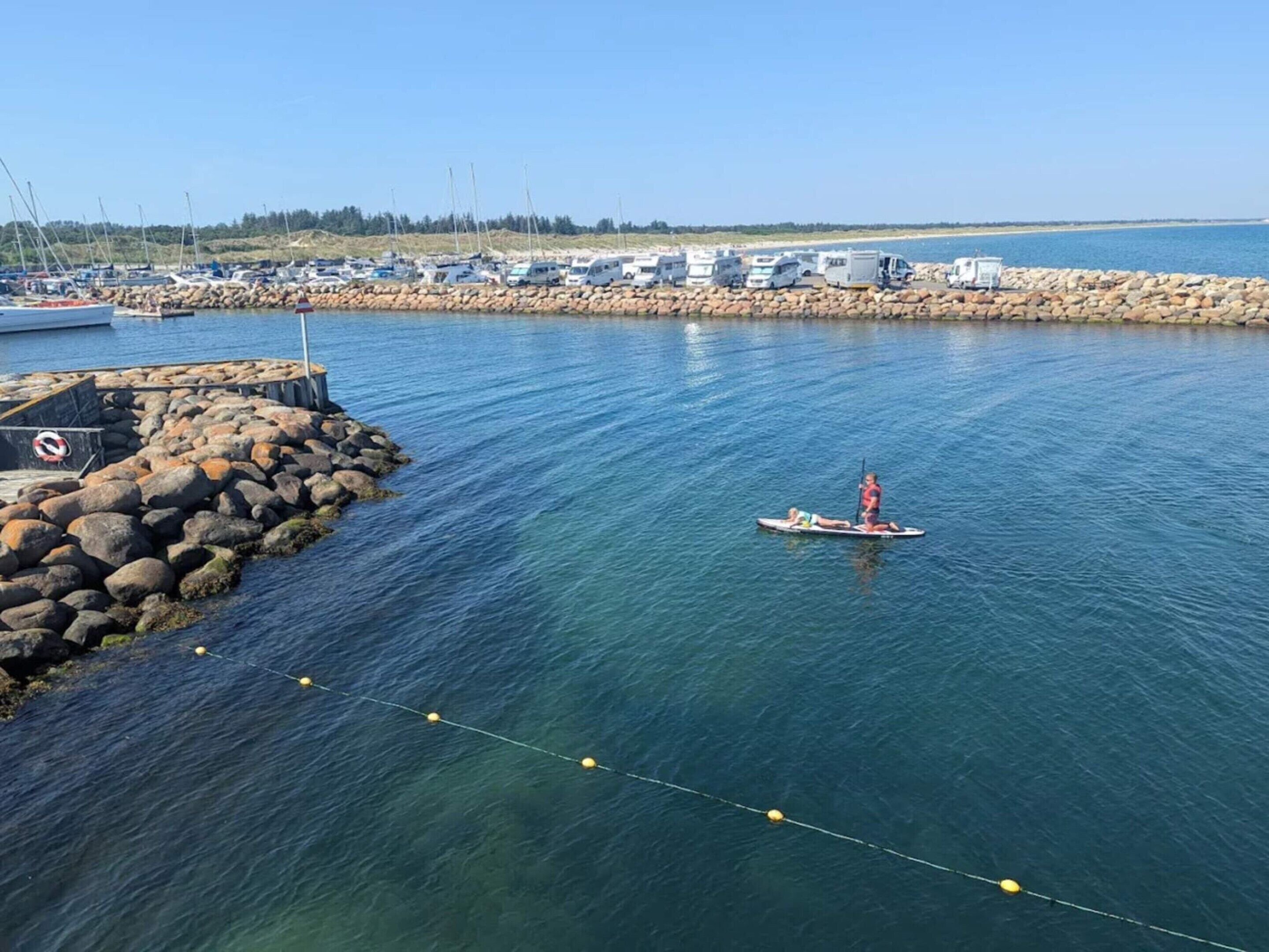 Un puerto deportivo con barcos amarrados, un rompeolas rocoso y una vía fluvial despejada.