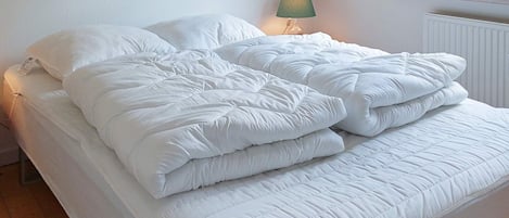 Una cama con ropa de cama blanca y una lámpara verde a su lado.