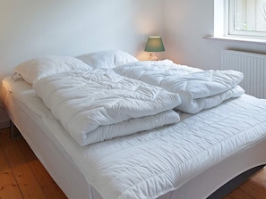 A bed with white bedding and a green lamp beside it.