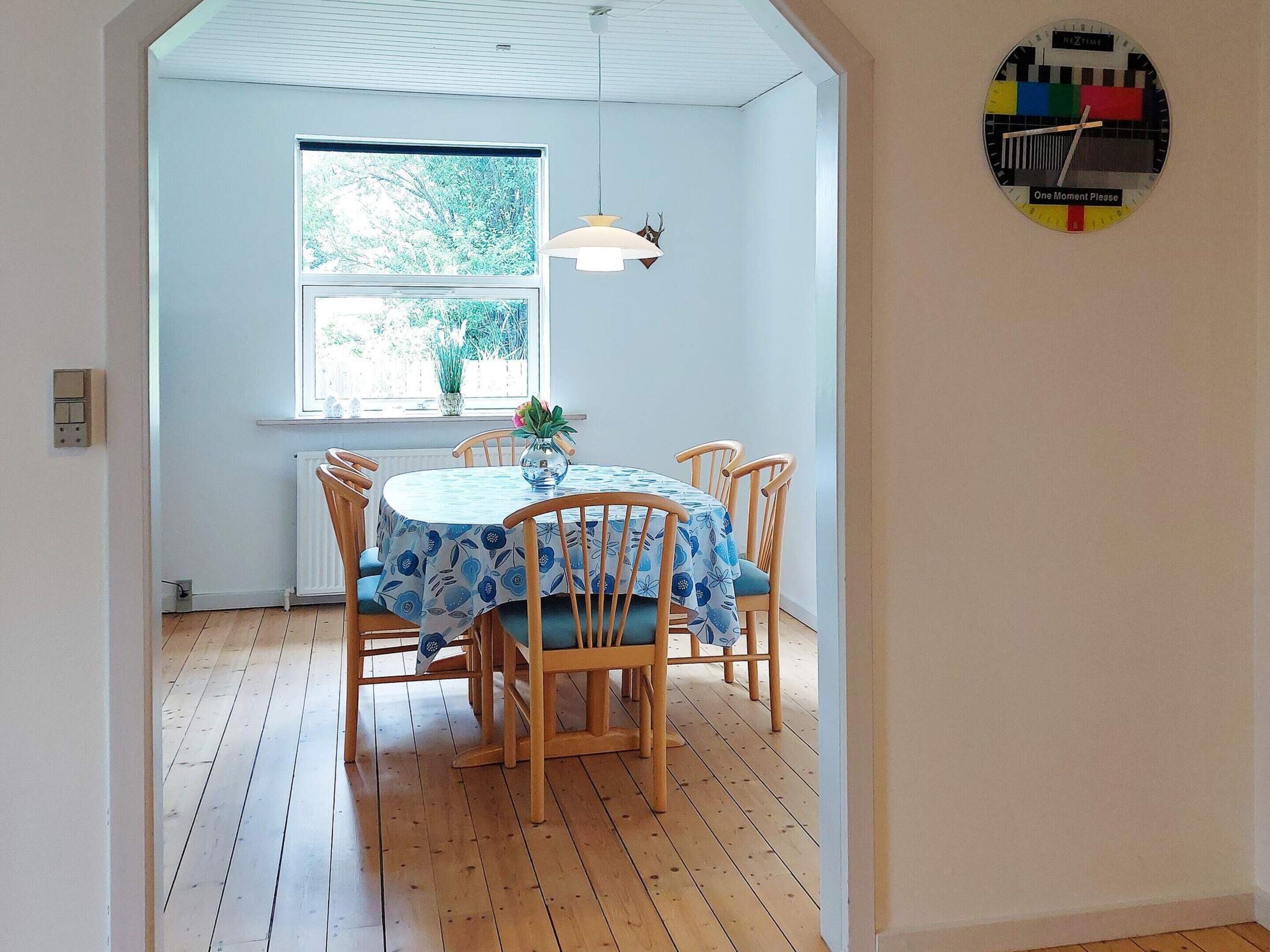 A dining area with a round table, chairs, a window, and a wall clock.