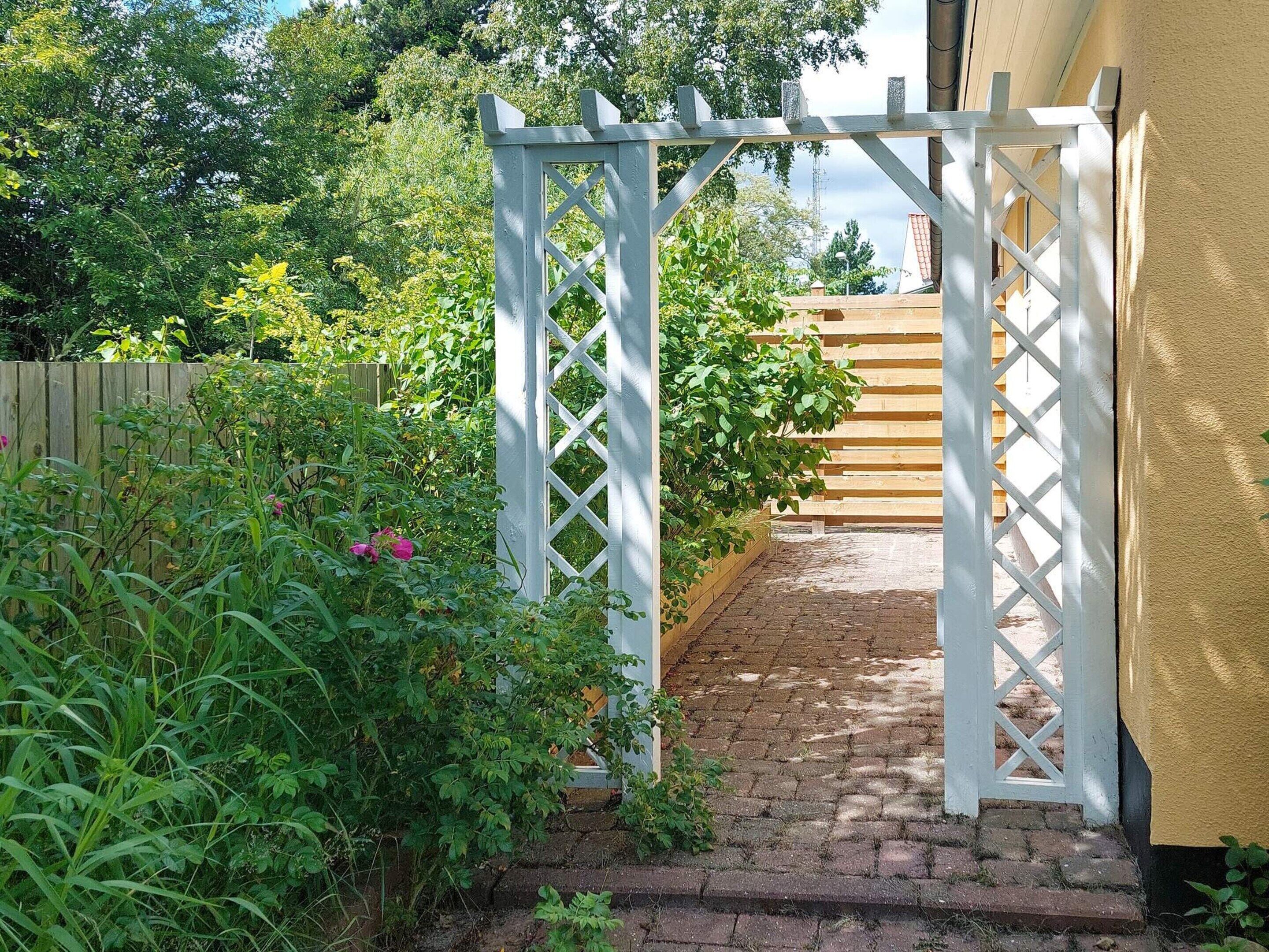 A garden pathway leading to a wooden gate, surrounded by lush greenery and a wooden fence.