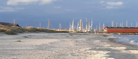 Une plage de sable avec des bateaux et un bâtiment rouge en arrière-plan.