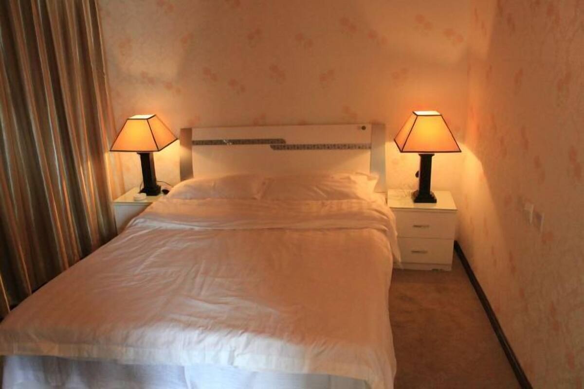 Ein ordentlich bezogenes Bett mit weißen Leinen, zwei Nachttischlampen und ein weißer Nachttisch mit einer Schublade.