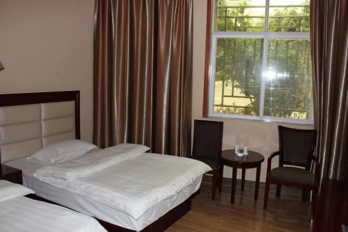 Ein Hotelzimmer mit zwei Betten, einem kleinen Tisch, zwei Stühlen und einem Fenster mit Vorhängen.